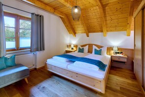 Ein Schlafzimmer mit Holzboden, einem Bett mit blauer Decke, einem Nachttisch mit Lampe und einem Fenster mit Vorhängen.