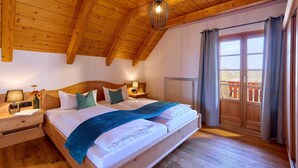 A wooden ceiling, a bed with pillows, a nightstand, a lamp, and a view through a window. - Vacation apartment Schlüsselblume, up to 4 persons, attic, 65 sqm (Waging am See)