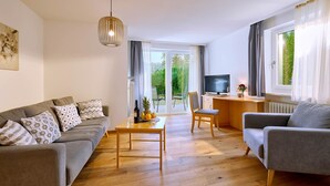 A living room with a sofa, armchair, wooden coffee table, and a TV. - Vacation apartment Gänseblümchen, up to 2 persons, first floor, 50 sqm (Waging am See)