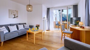 Ein modernes Wohnzimmer mit Sofa, Esstisch, Fernseher und Blick ins Freie.
