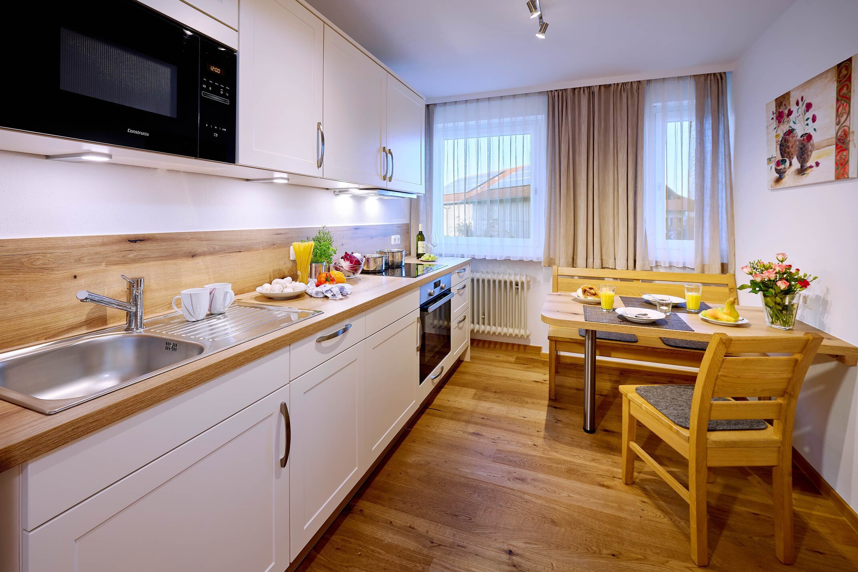 Eine moderne Küche mit Mikrowelle, Spüle und Holzarbeitsplatte. Ein Essbereich mit Tisch und Stühlen ist vorhanden, sowie ein Fenster mit Vorhängen.