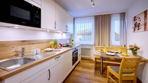 Eine moderne Küche mit Mikrowelle, Spüle und Holzarbeitsplatte. Ein Essbereich mit Tisch und Stühlen ist vorhanden, sowie ein Fenster mit Vorhängen.