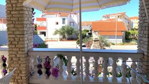 A balcony with stone pillars, a striped umbrella, and a view of buildings with red roofs. - Tremendous 2-bedroom Apartment with AC in tranquil Vodice (Vodice)