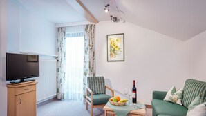 En stue med fjernsyn, en stol, en sofa, et bord med frugt og vin, samt et billede på væggen.
