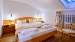 Un dormitorio con cama de madera, mesitas de noche, una silla, un tragaluz y un ventanal con cortinas.