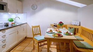Una cocina con una mesa de comedor, sillas, microondas, armarios, un reloj y una planta pequeña.