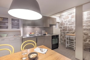 A modern kitchen with grey cabinets, a wooden dining table, and a stone wall.