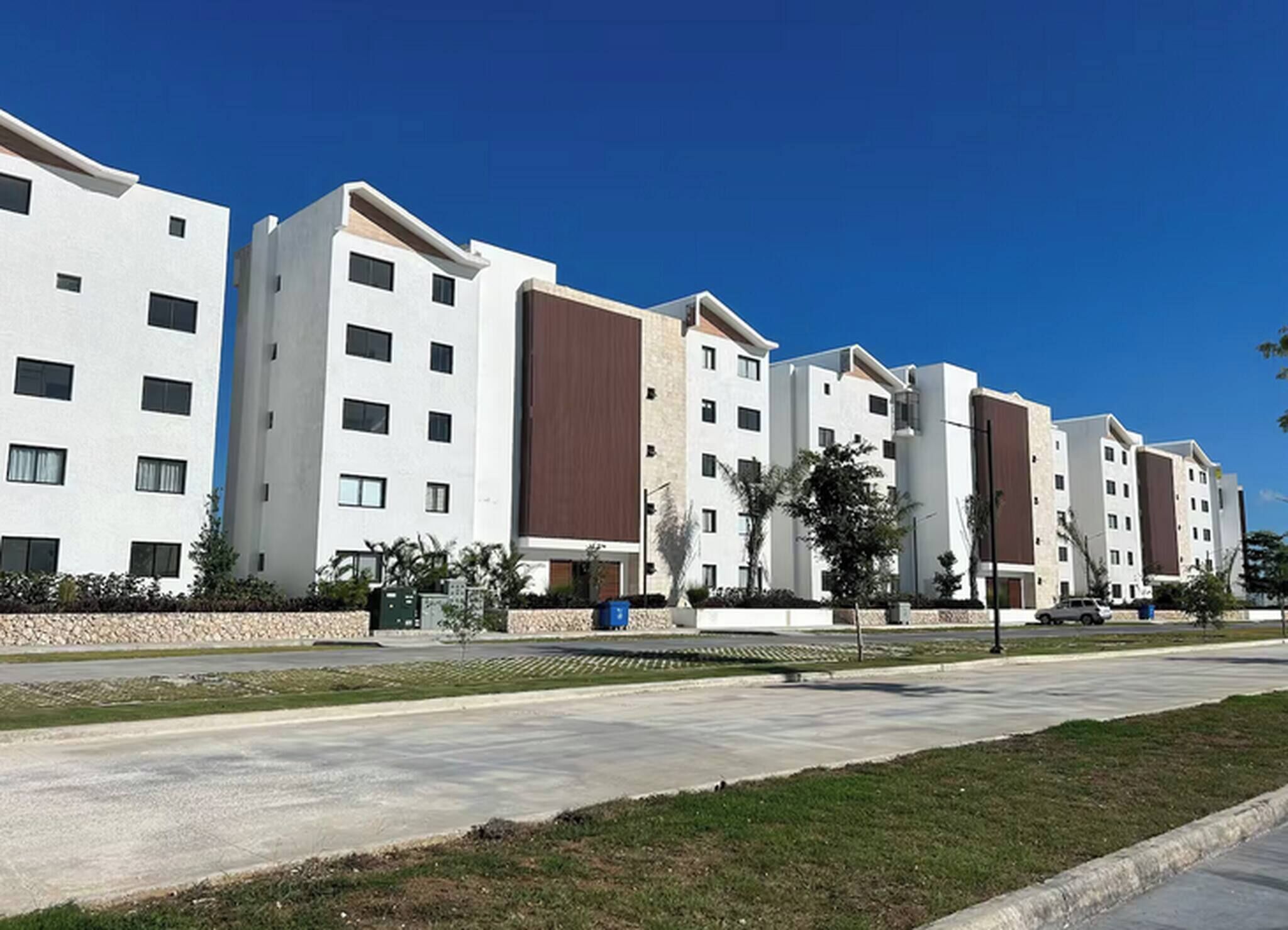 Eine Reihe moderner Apartmenthäuser mit flachem Dach, einem Innenhof und einem strahlend blauen Himmel.