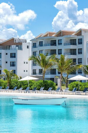A hotel with a pool, sun loungers, palm trees, and a boat. - Modern 2bdrm Apt Lagoon-style Beach Downtown (Punta Cana)