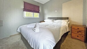 Quarto com cama, janela com persiana, mesa de cabeceira e cómoda de madeira.