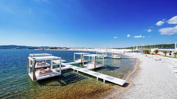 Ein Strand mit klarem Wasser, weißen Cabanas und einer Marina mit Booten.