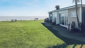 Una propiedad costera con césped, un patio con sillas y vista al mar.