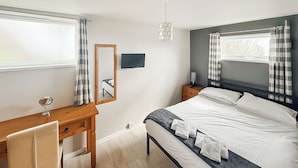 Ein Schlafzimmer mit Bett, Nachttisch, Spiegel, Schreibtisch mit Stuhl und einem Fenster mit Vorhängen.