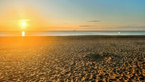 Ein Strand bei Sonnenuntergang, ruhige See und im Hintergrund Windkraftanlagen.