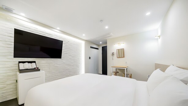 Ein modernes Hotelzimmer mit einem großen Bett, einem flachbildfernseher an der Wand, einem Nachttisch mit Lampe und einem kleinen Schreibtisch mit Stuhl.