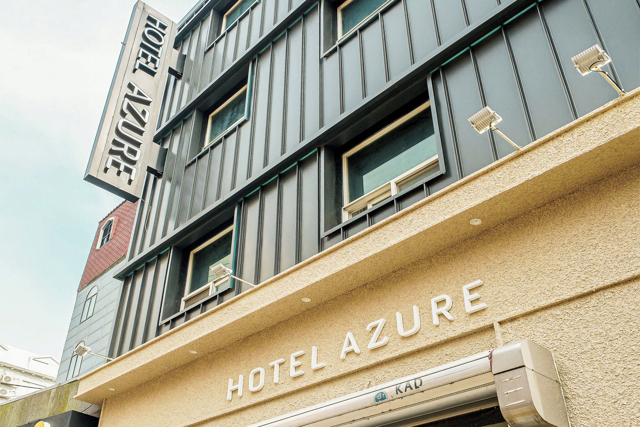 Fachada de hotel com uma placa indicando 'HOTEL AZURE' e uma janela visível.