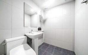 Un baño moderno con inodoro, lavabo, espejo, ducha y piso cubierto de baldosas oscuras.