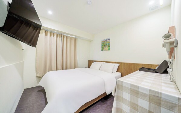 Habitación de hotel con cama, mesita de noche con teléfono, secador de pelo en la pared y ventana con cortinas.