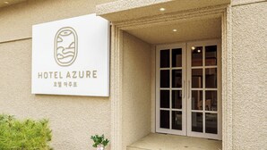 Ein Hotel Eingang mit einem Schild, auf dem 'HOTEL AZURE' steht, und einer Glastür.