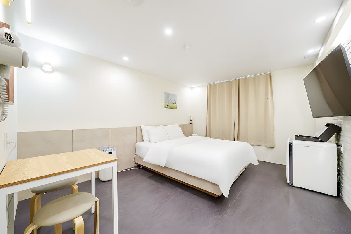 Una habitación de hotel con cama, escritorio, silla, televisor y un mueble pequeño.