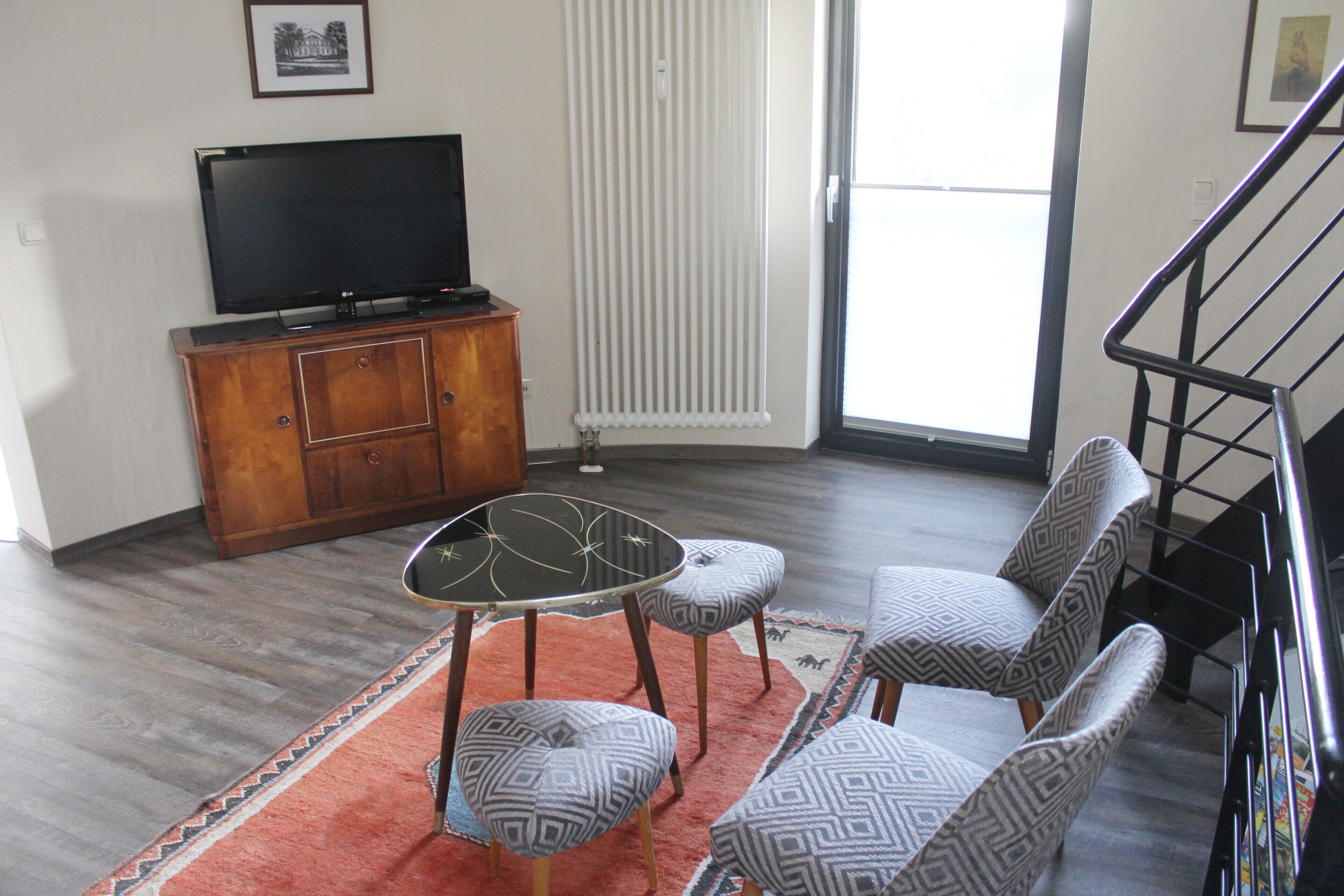 Un salon avec un téléviseur, un meuble en bois, des fauteuils à motifs et un tapis rouge.