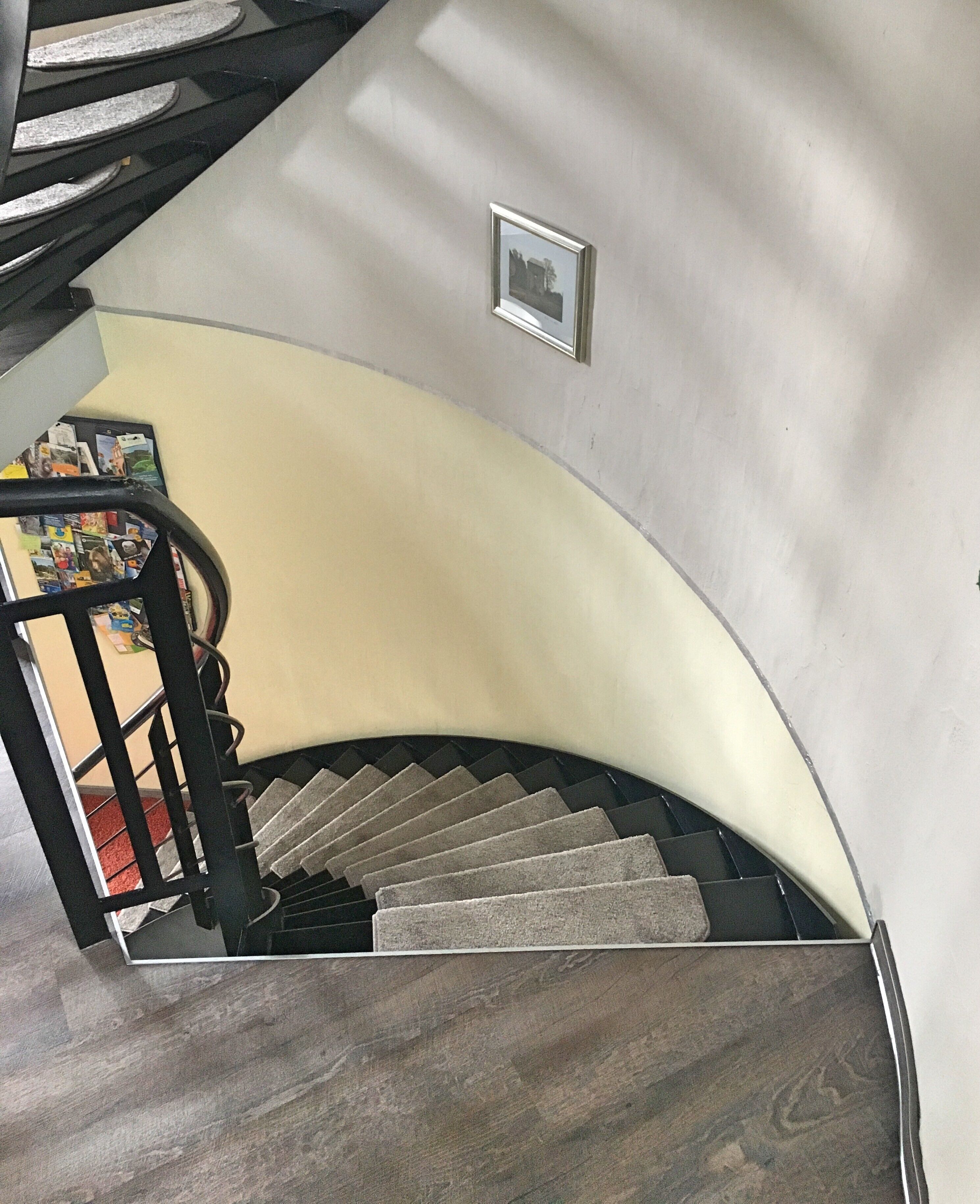 Een gebogen trap met een leuning, bekleed met tapijt, en een aan de muur bevestigd schilderij.