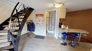 Un escalier, un porte-manteau, un coin bar avec des tabourets et une affiche au mur.