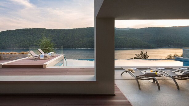 Zona junto a la piscina con sillones de descanso y vistas a un lago y colinas boscosas.