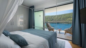 Un dormitorio con una cama grande, un balcón con vistas a un lago y colinas, y una mesa con dos vasos.