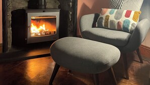 A cozy room with a fireplace, a chair with a colorful cushion, and a map on the wall. - The Old School Glasfryn | Dog Friendly | Betws y Coed 15 min | Ideal for Snowdon (Glasfryn)