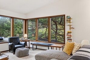 Ein gemütliches Zimmer mit einem großen Fenster, einer Bank, einem Sessel, einem kleinen Tisch und einem Bücherregal.