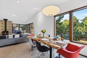 A modern dining area with a long table, chairs, and a view of the outdoors. - Movie Room + Fire Pit + Deck with Views + Walk to the Beach | Magic Tree House (Manzanita)