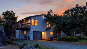 A two-story house with a balcony, a garage, and a driveway. - Movie Room + Fire Pit + Deck with Views + Walk to the Beach | Magic Tree House (Manzanita)