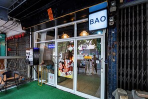 A BAO establishment with a glass door entrance, a small outdoor seating area with chairs, and a visible signboard. - BAO The Giant Swing (Bangkok)