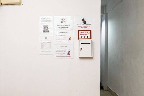 En væg med forskellige informationsplakater, inklusive en QR-kode, Wi-Fi adgangskode, rengøringsinstruktioner og et skilt med information om nøglegivning.