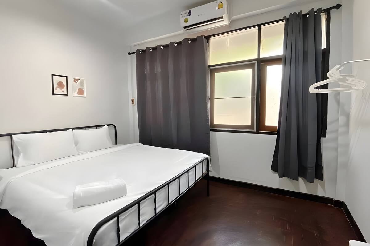 Ein Hotelzimmer mit Bett, Klimaanlage, Fenster mit Vorhängen und Kleiderhaken.