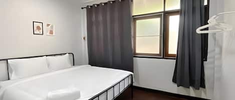 A hotel room with a bed, an air conditioning unit, a window with curtains, and a coat rack.
