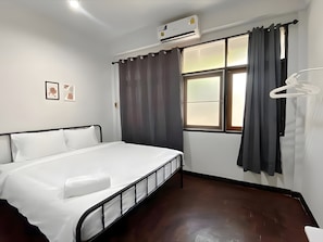 Une chambre d’hôtel équipée d’un lit, d’un appareil de climatisation, d’une fenêtre avec des rideaux et d’un porte-manteau.