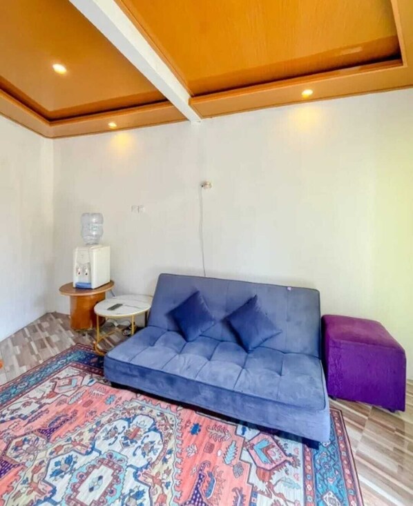 A room with a blue sofa, a purple ottoman, a patterned rug, a water dispenser, and a small table.