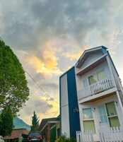 Un edificio de varios pisos con un balcón, un letrero que indica un negocio, y un cielo despejado con nubes.