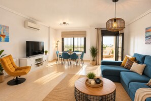 Una sala moderna con sofá, televisión, comedor y balcón con vistas.