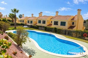 Una piscina rodeada de un jardín ajardinado, con una hilera de edificios amarillos al fondo.