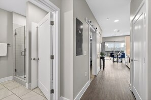 A modern hallway with a glass shower, white doors, and a dining area with blue chairs. - Hillsboro Village Studio + Balcony | Near Vanderbilt, Belmont, Music Row (Nashville)