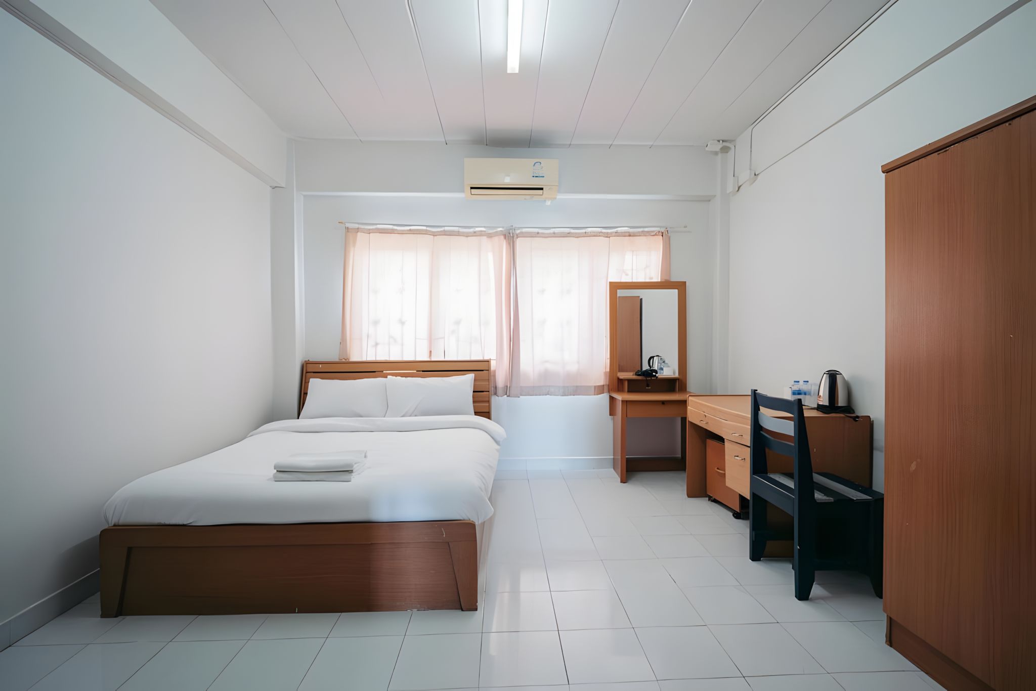 A hotel room with a bed, a desk, a chair, a wardrobe, and a window with curtains.