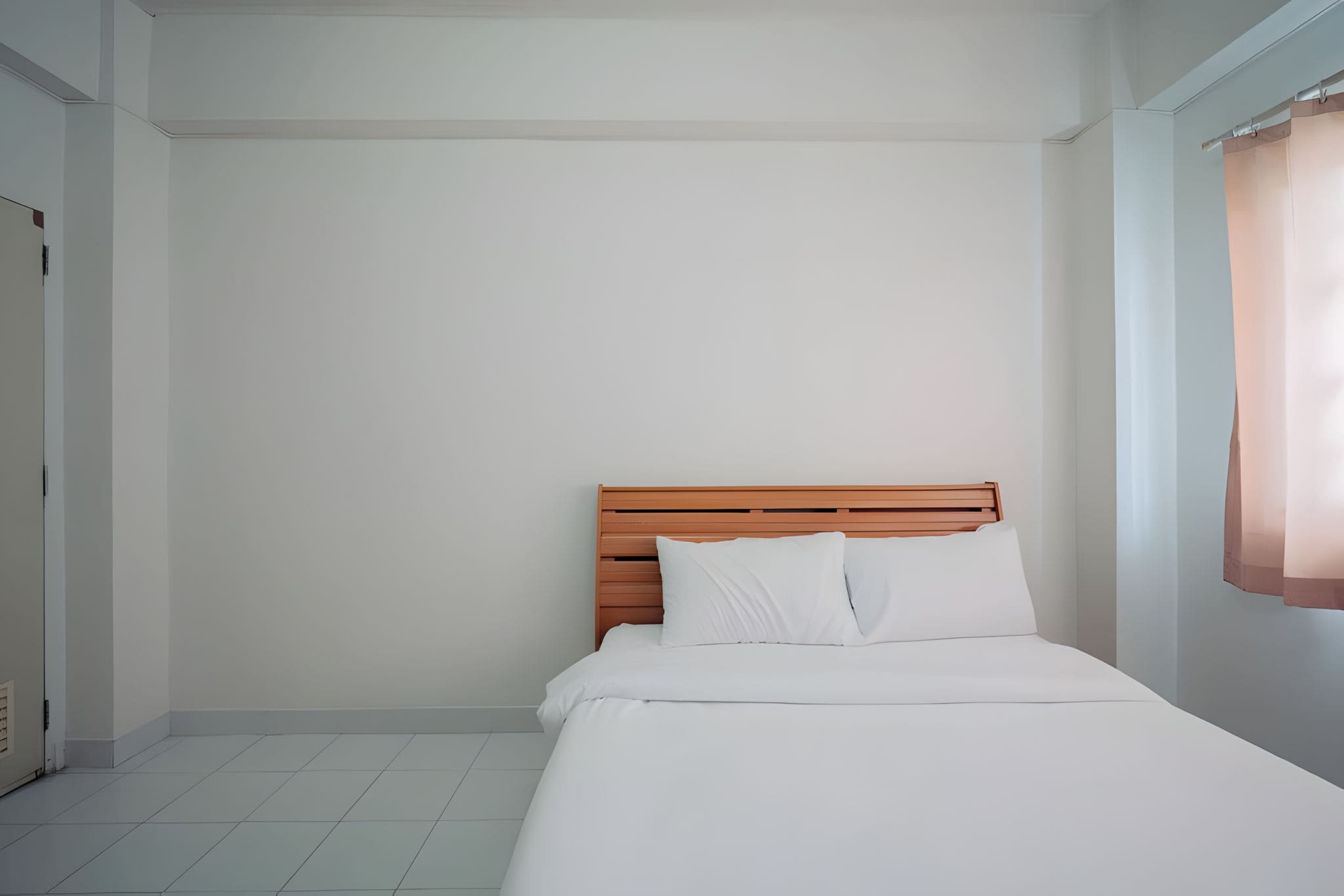 Una cama individual con cabecera de madera en una habitación con paredes blancas y suelo de baldosas.