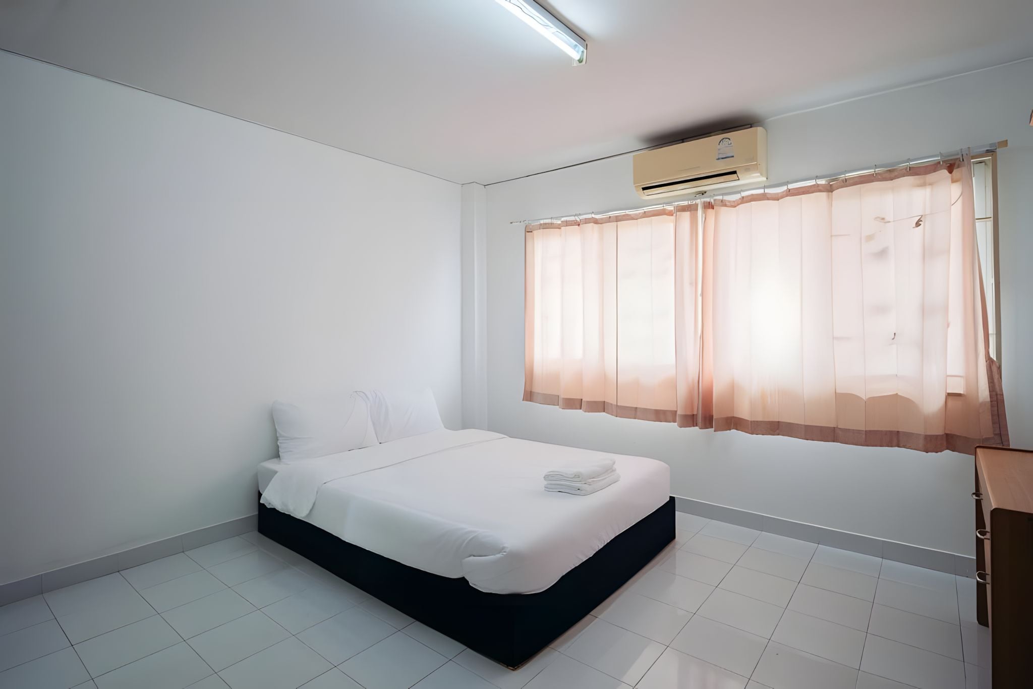 Ein Schlafzimmer mit Bett, weißen Wänden, einem Fenster mit durchsichtigen Vorhängen und einer Klimaanlage.