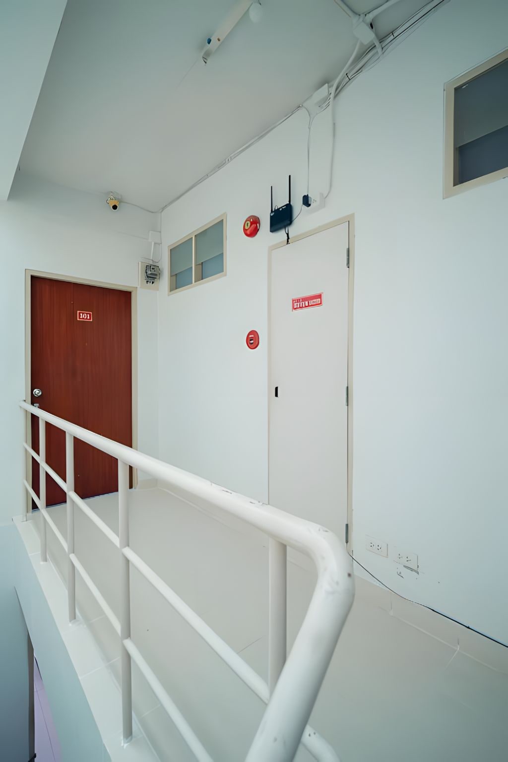 A staircase with a white handrail, a wooden door labeled '101', and a fire alarm on the wall.