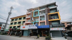 Un immeuble à plusieurs étages, avec différentes boutiques en rez-de-chaussée, dont un salon de coiffure et un magasin dont l’enseigne est rédigée dans une langue étrangère.