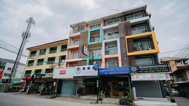 A multi-story building with various storefronts, including a hair salon and a shop with a sign in a foreign language. - Oh My Nap Bangsaen (Chonburi)