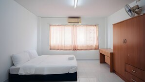 A bedroom with a bed, a desk, a wardrobe, a window with curtains, and an air conditioning unit. - Oh My Nap Bangsaen (Chonburi)